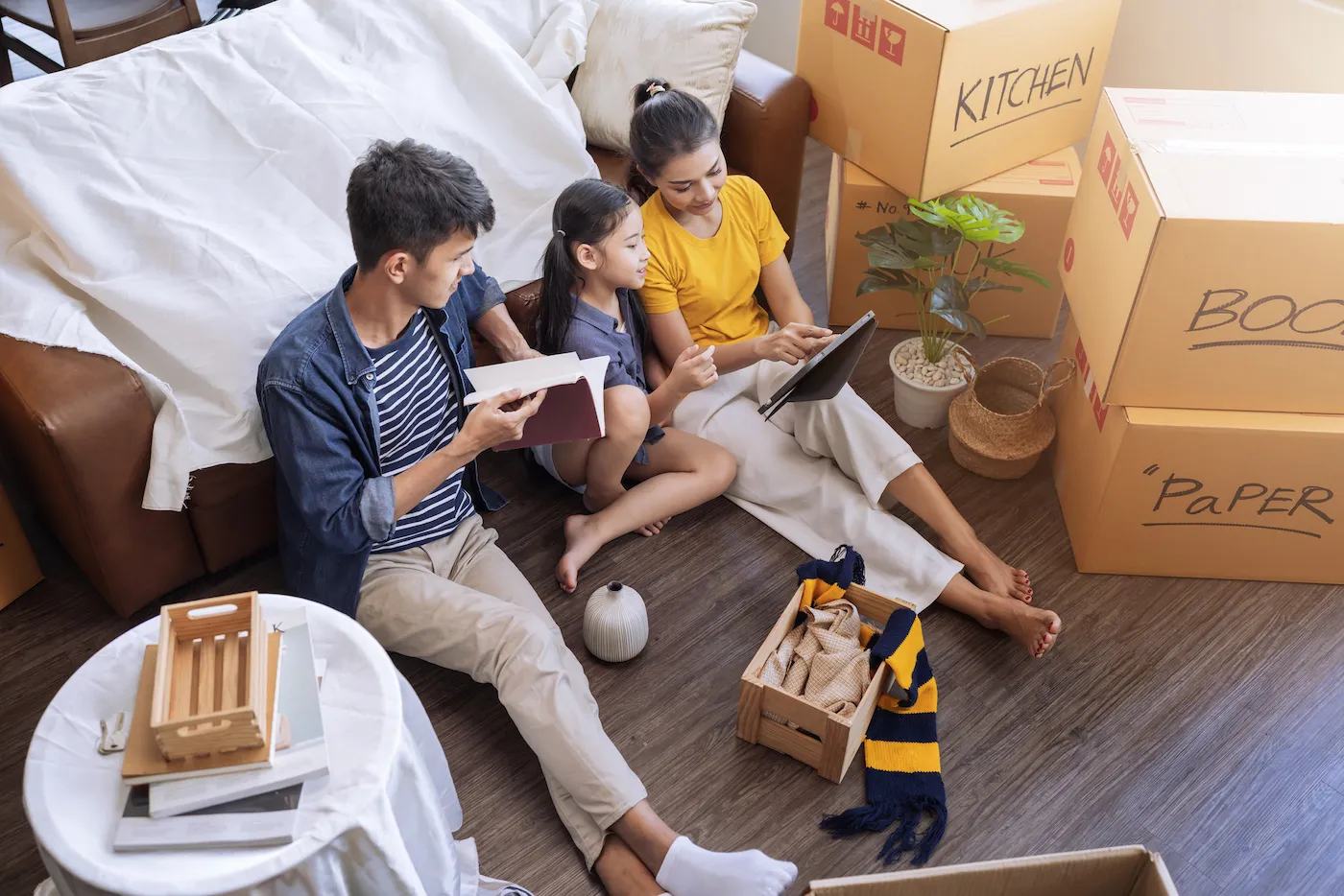 A family sitting on the floor, packing up their home to rent it and buying another