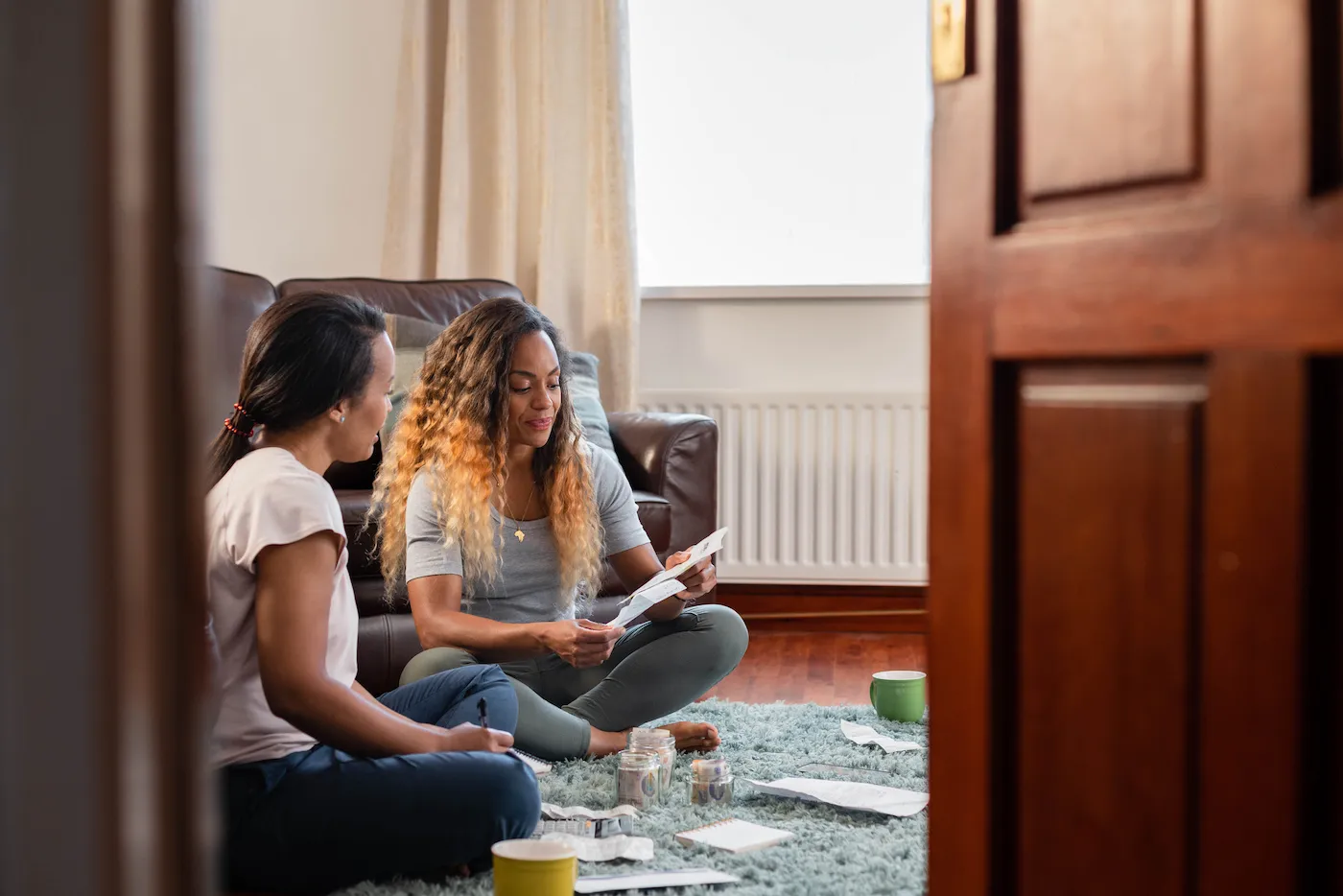 Two friends going through personal finances at home. They are smiling at each other positively. Shot through a doorway