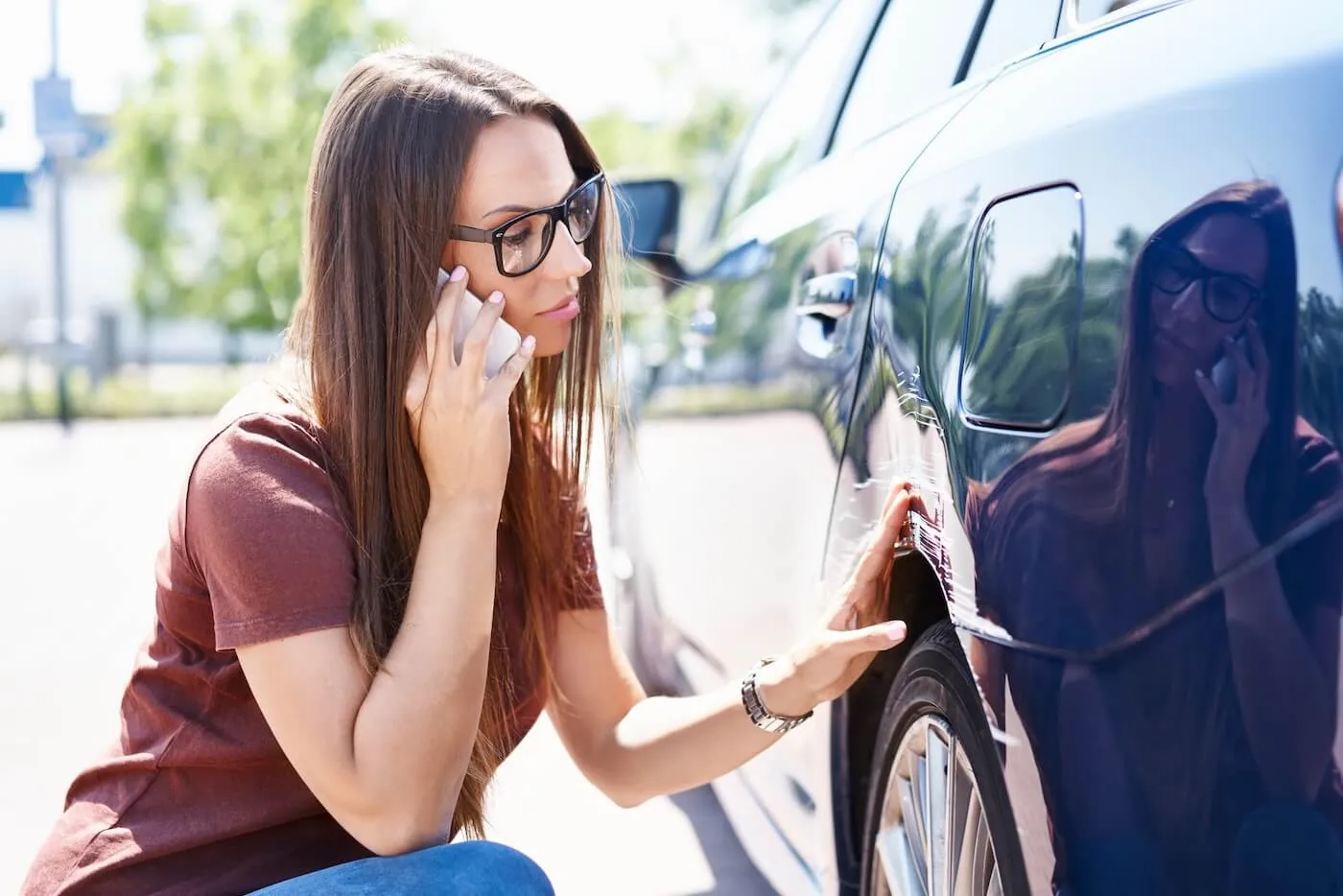 Woman is calling her insurance company after a minor car accident while checking the scratches on her car