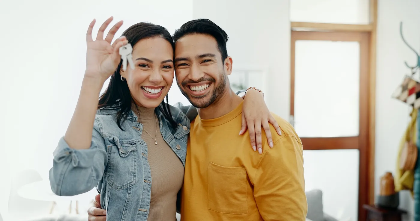 A smiling couple embracing and holding the keys to their new home.