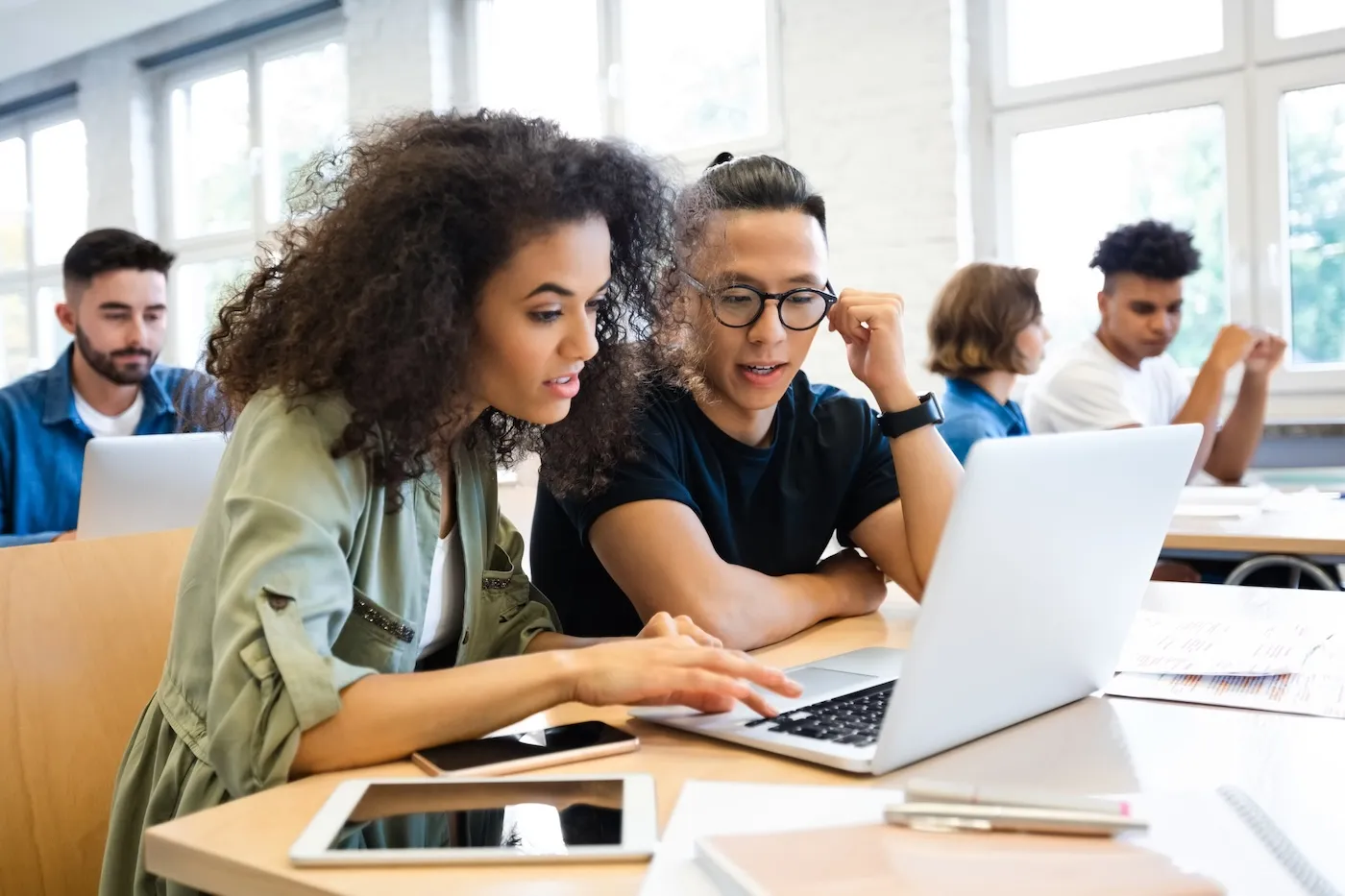 Two college students researching student loans on a laptop in class together.