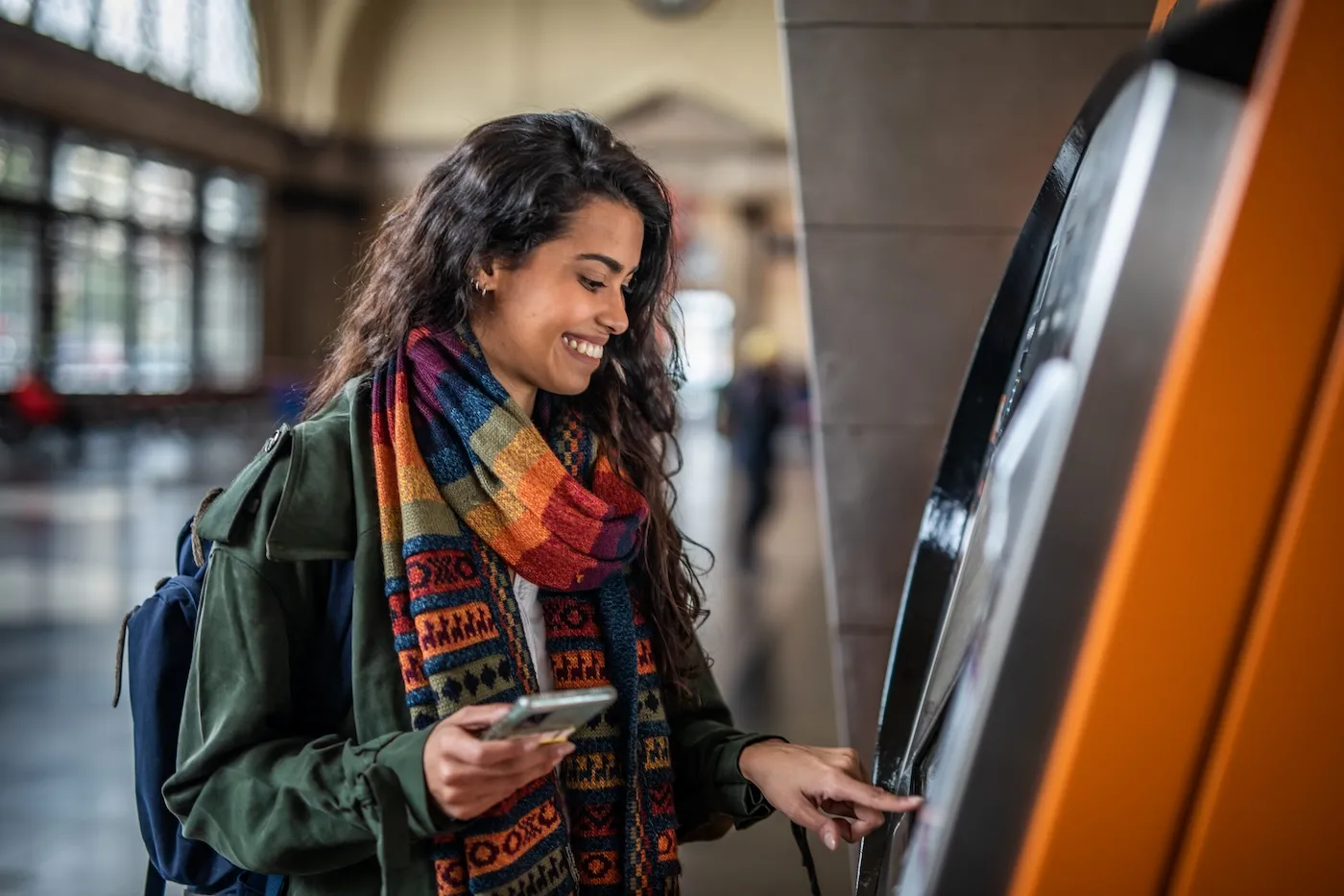 A casually dressed young woman using an ATM in a metro station in Barcelona to withdraw her money.