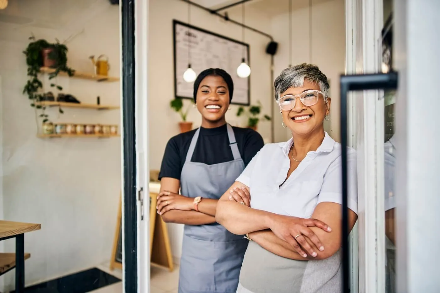 Two smiling women in aprons standing next to their small shop