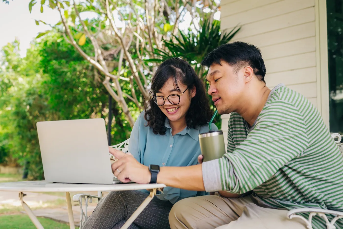 Happy young couple using laptop computer while sitting in front of the house, Couple relaxing and spending time together in backyard at home.