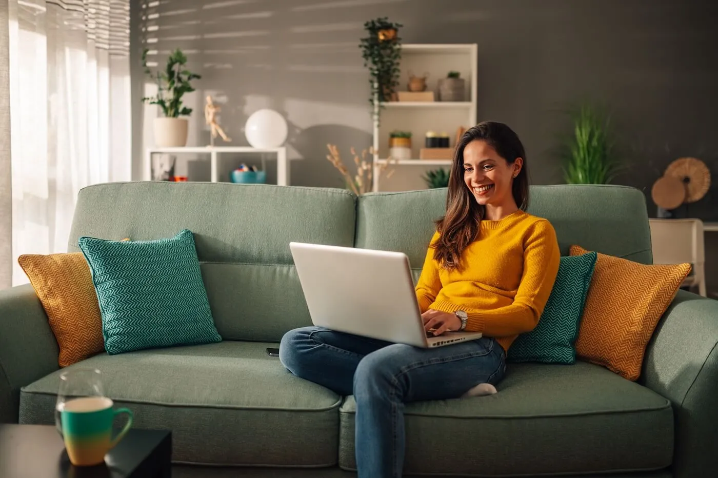 A smiling woman sitting on the couch with her laptop