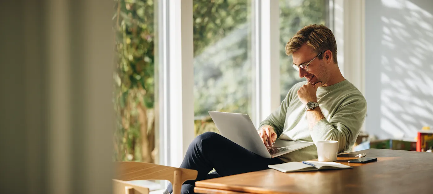 Young man using laptop and smiling at home. Man sitting by table working on laptop computer.