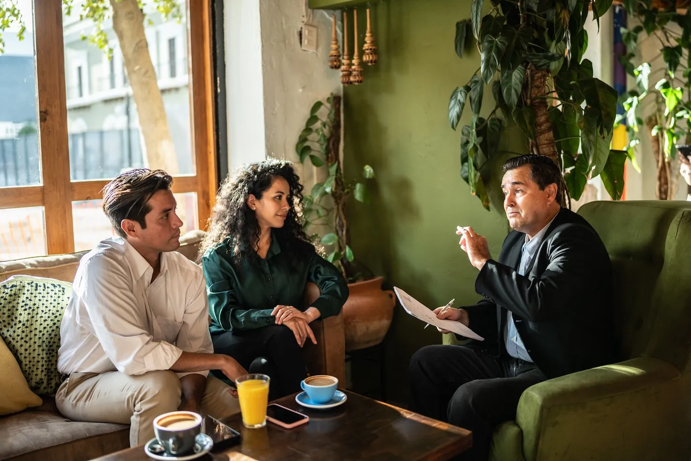 Mid adult couple having a meeting with a financial advisor in their green sunny living room.