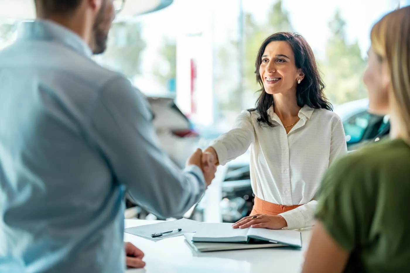 Smiling female agent shaking hands with the couple after signing an auto loan agreement in the dealership