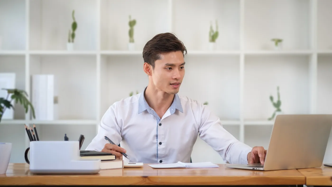 Young man using laptop and doing some paperwork at his personal office.