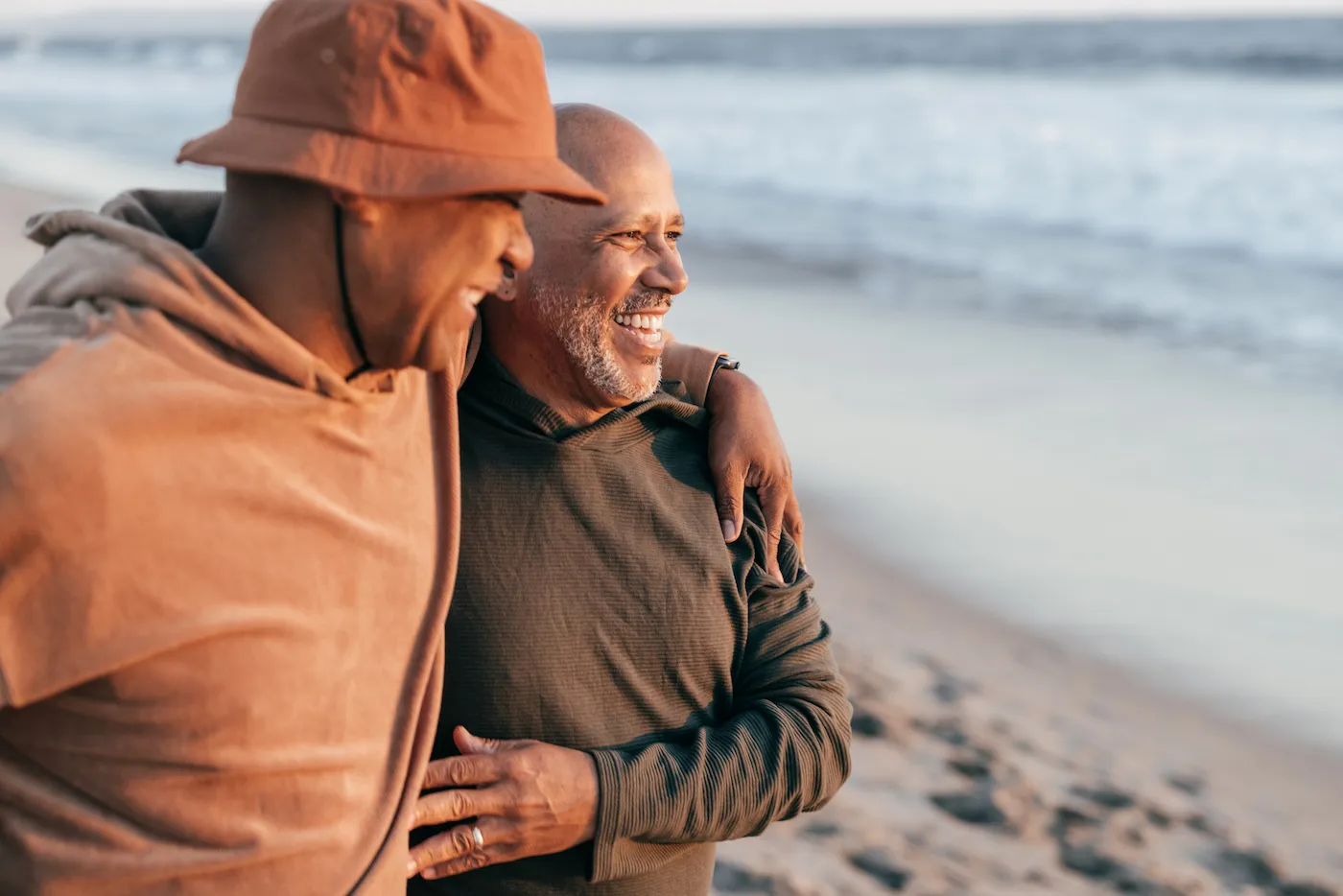 Senior couple on the beach, embracing and looking into the sunset above the ocean horizon.