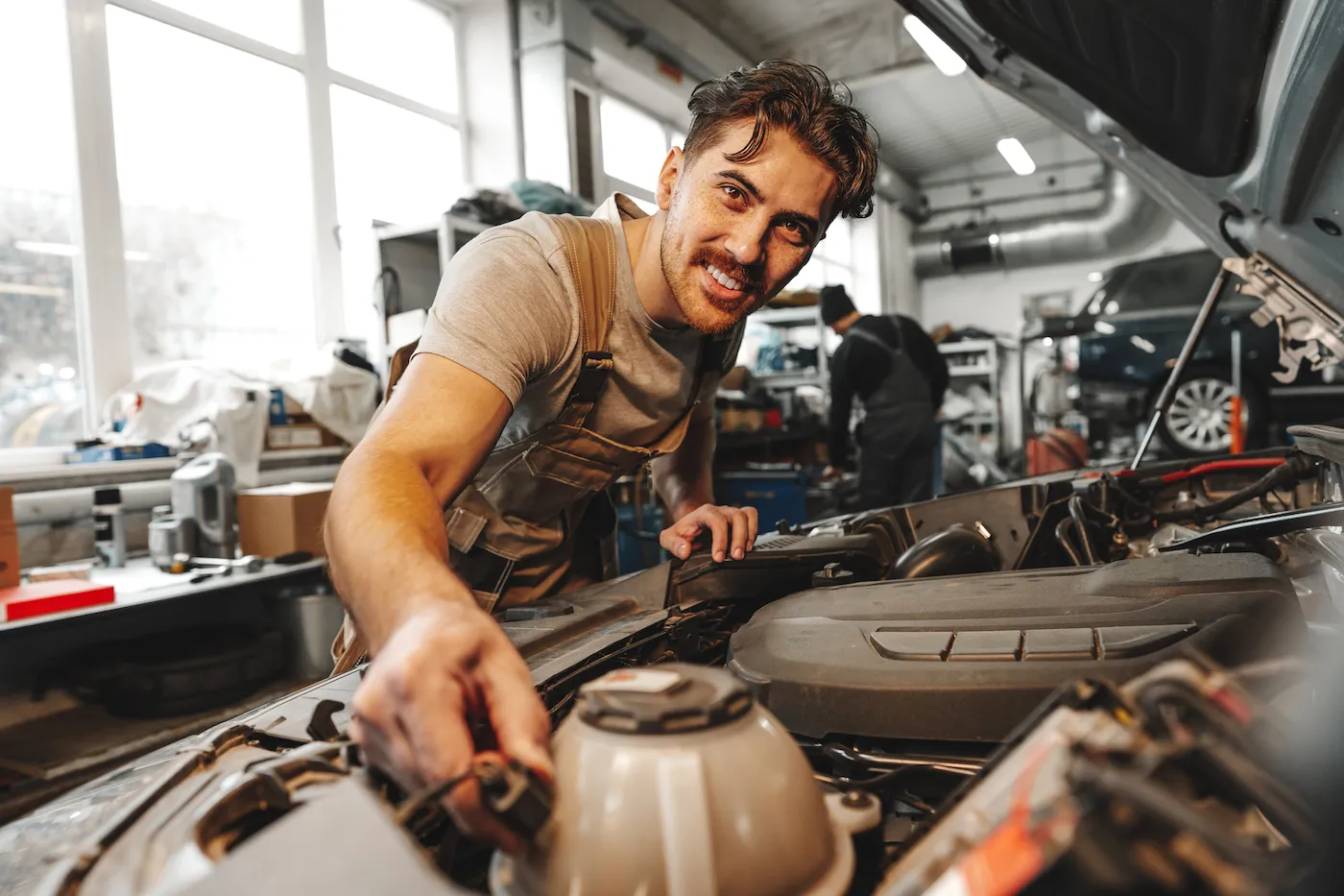 Young male mechanic examining engine under hood of car at the repair garage.