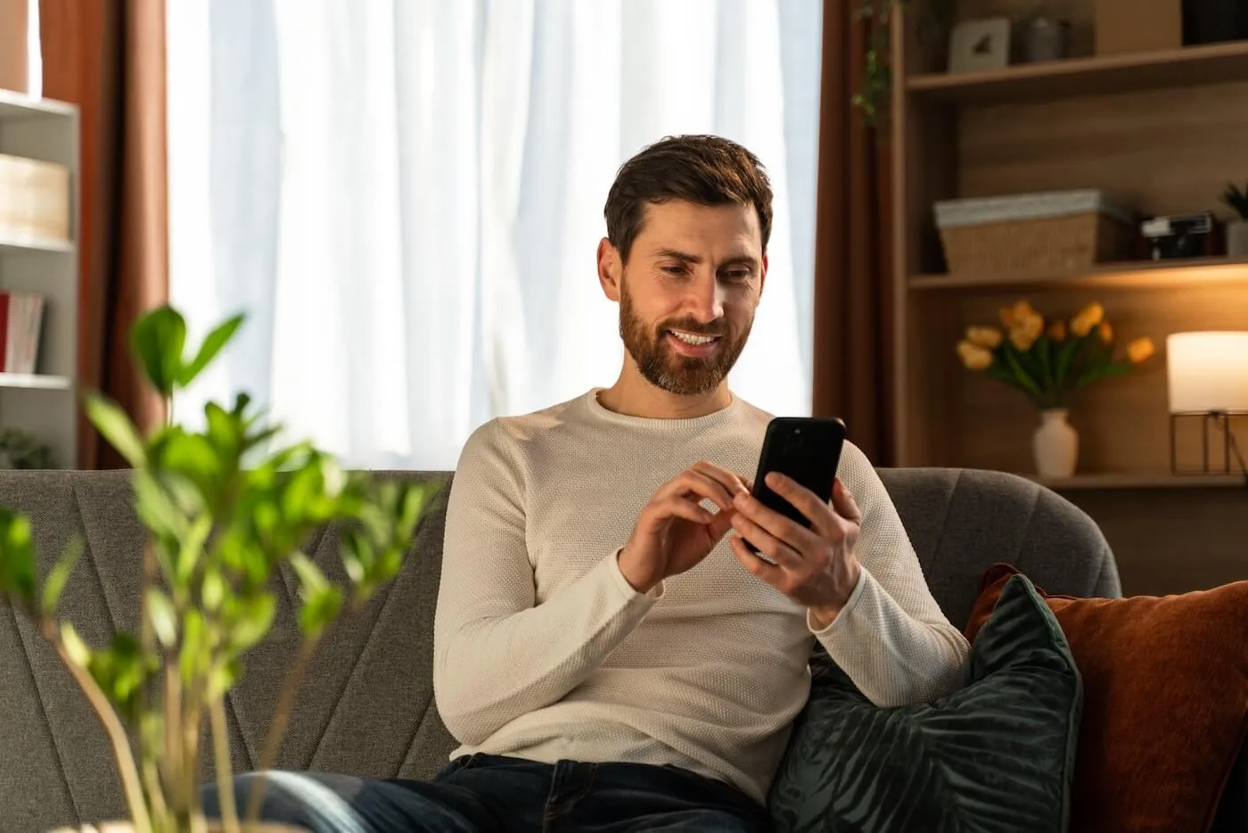 Smiling man using his smartphone while sitting on a sofa