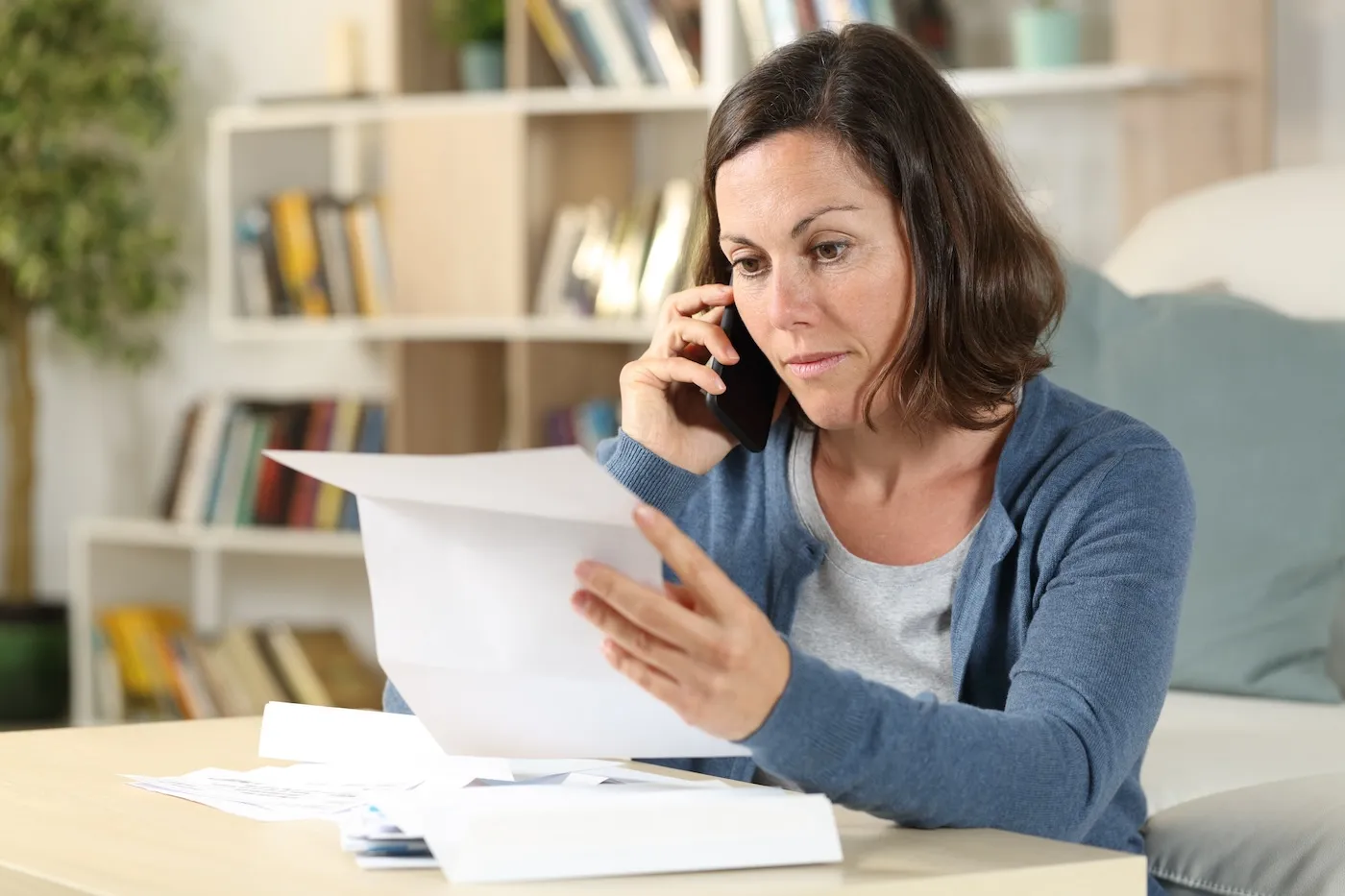 Serious adult woman checking letter calling on phone at home.