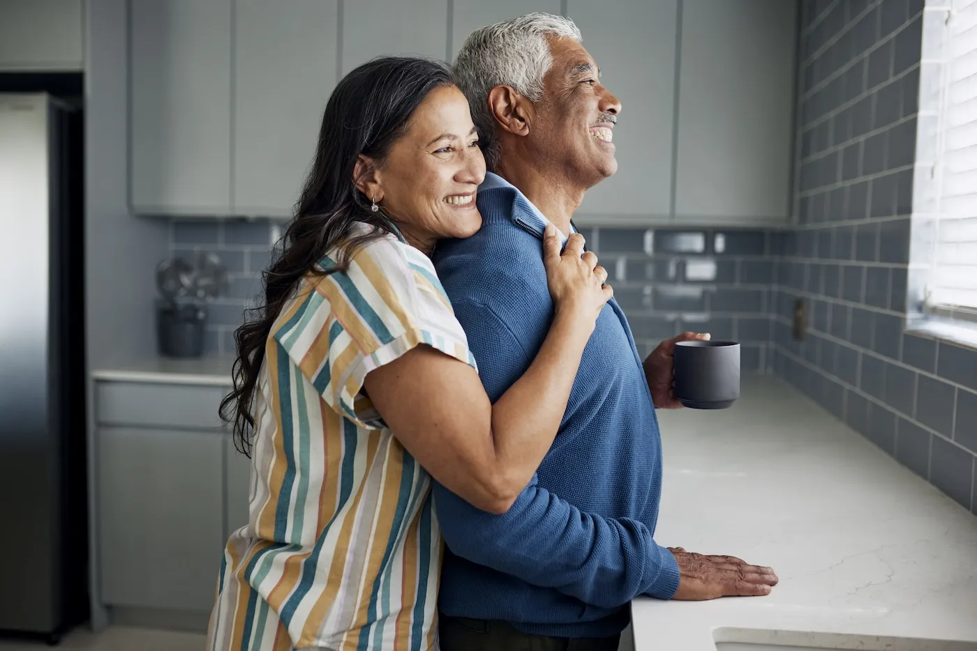 An elderly couple is drinking coffee and gazing out the kitchen window.