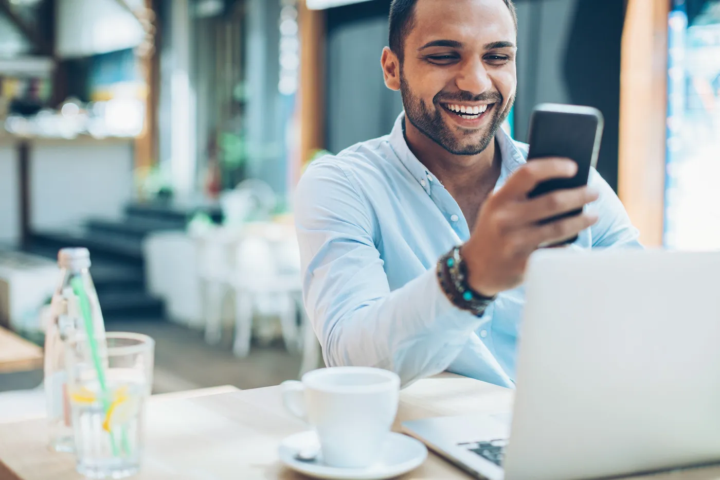 Smiling man sitting in cafe and checking investments, with his laptop in front of him.