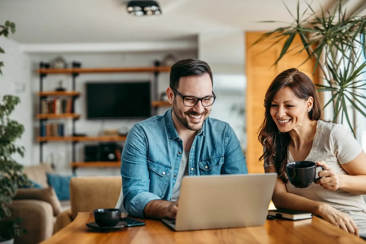 Happy couple using the laptop in the home office while drinking coffee