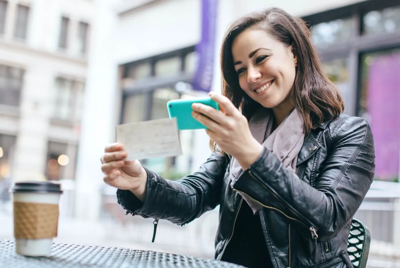Smiling young woman depositing a check via mobile app in the outdoor cafe