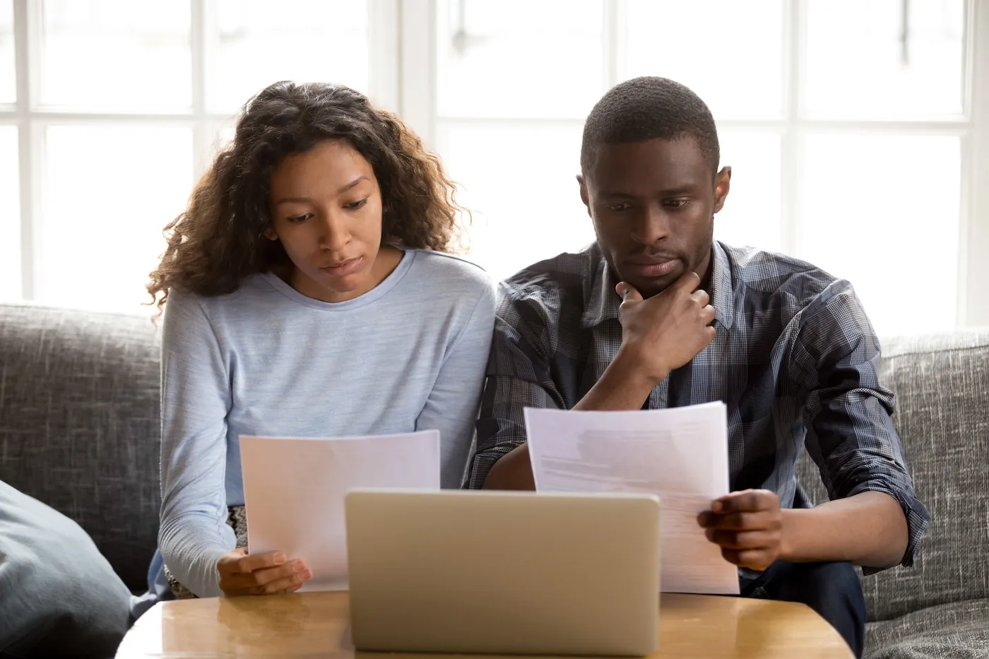 Serious focused couple reading paper banking documents, sitting together on the couch at home.