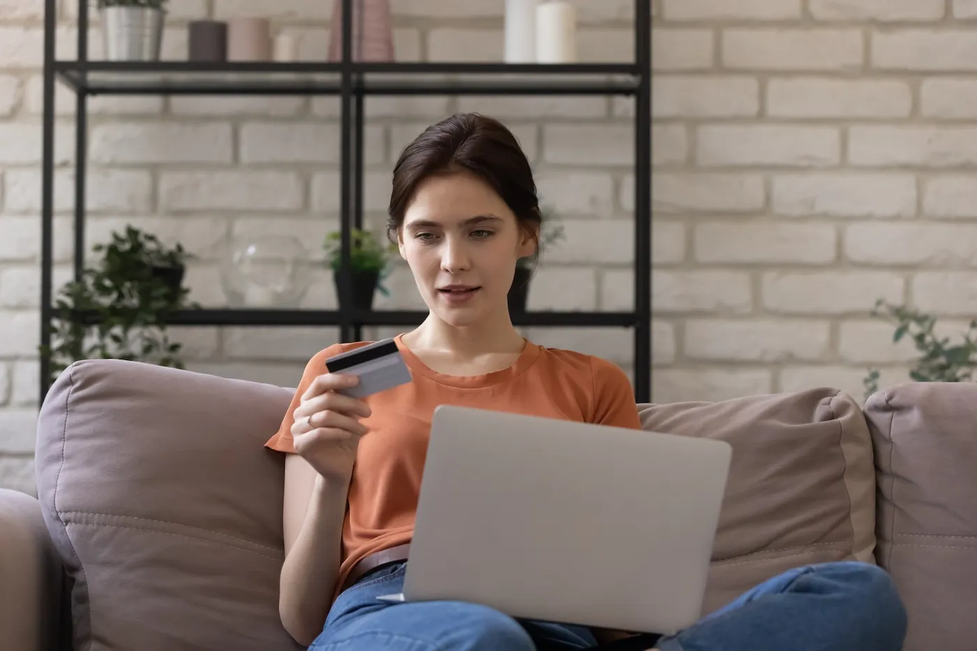 Young woman sitting on couch at home on laptop using credit card.