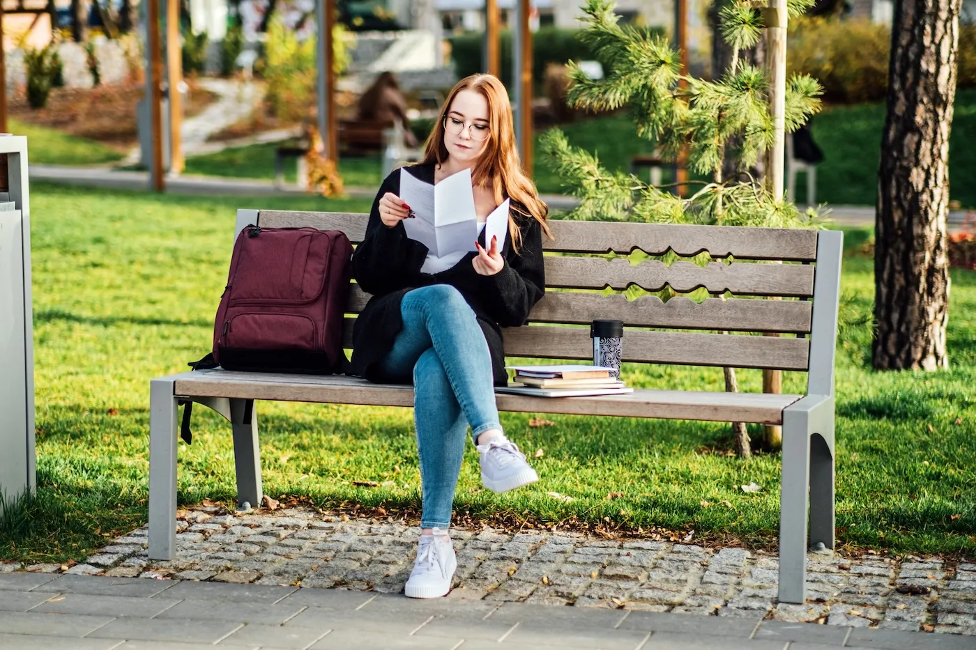 A new graduate sitting on a bench in the park with her backpack, holding a letter. She is understanding Student Loan Repayment Options.