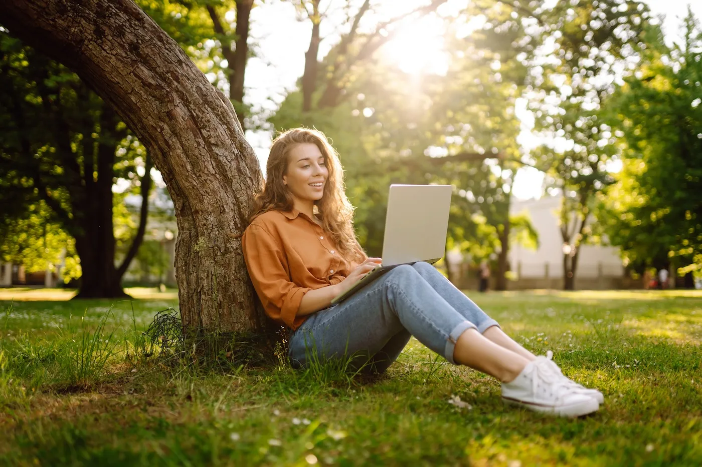 A woman in casual clothes on a green lawn with a laptop.