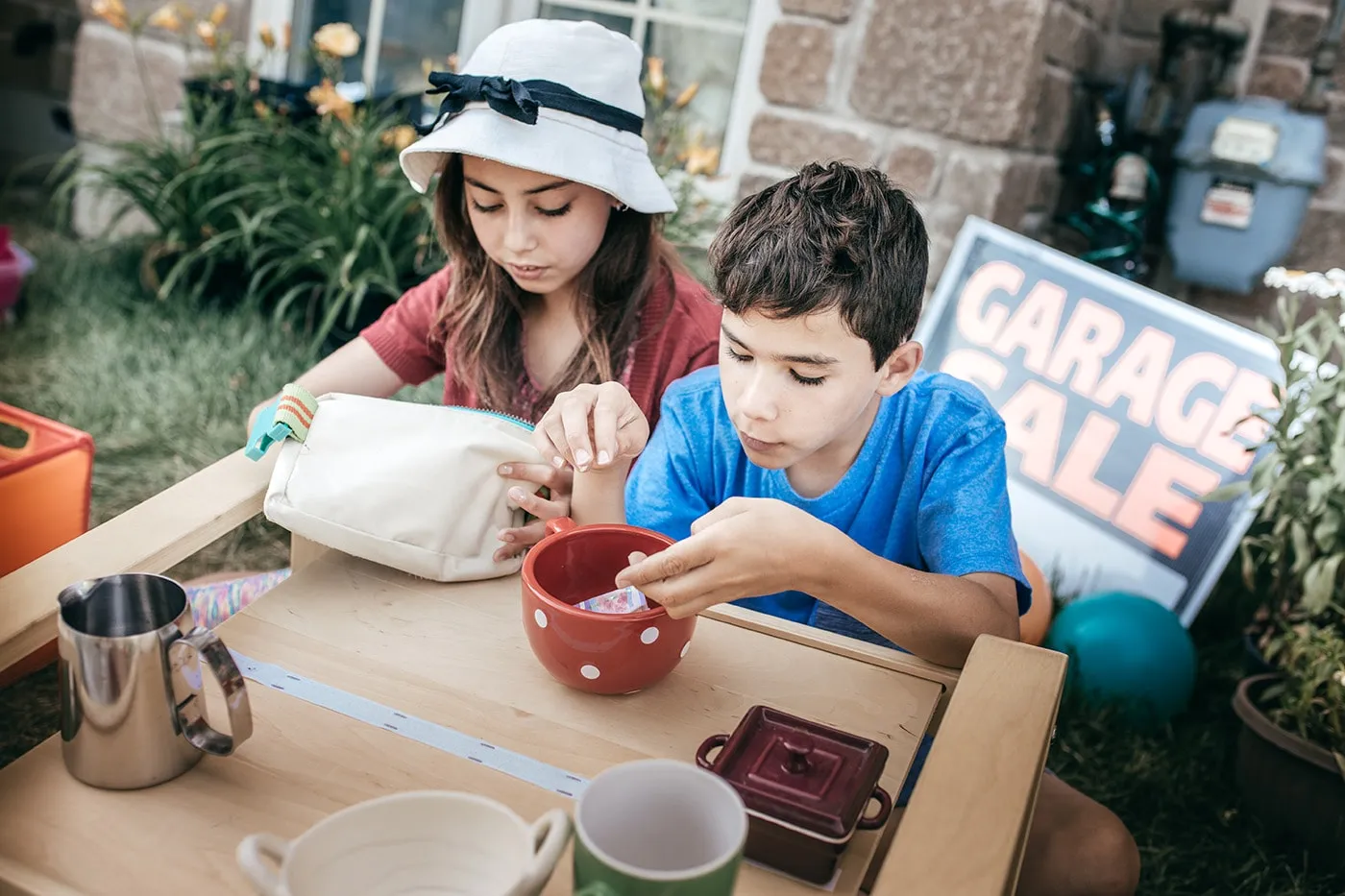 Two kids sitting at a table and counting coins at a garage sale.