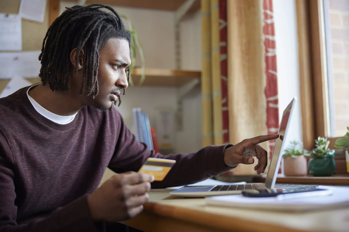 Man looking at laptop holding credit card with concerned look on his face.