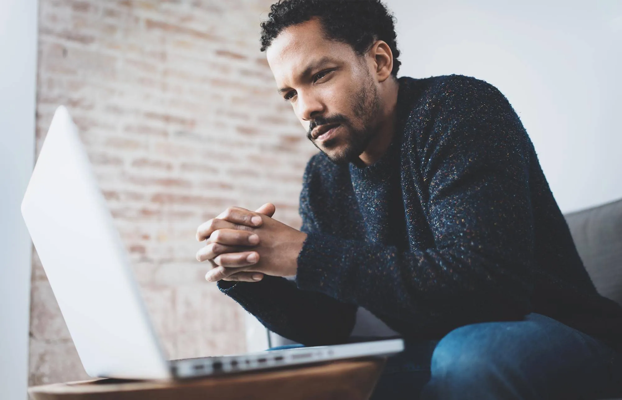 man in dark long sleeve holding hands and lookin pensive at laptop screen