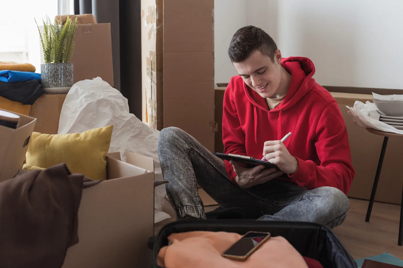 Cheerful young man smiling when writing a checklist to save money for college.