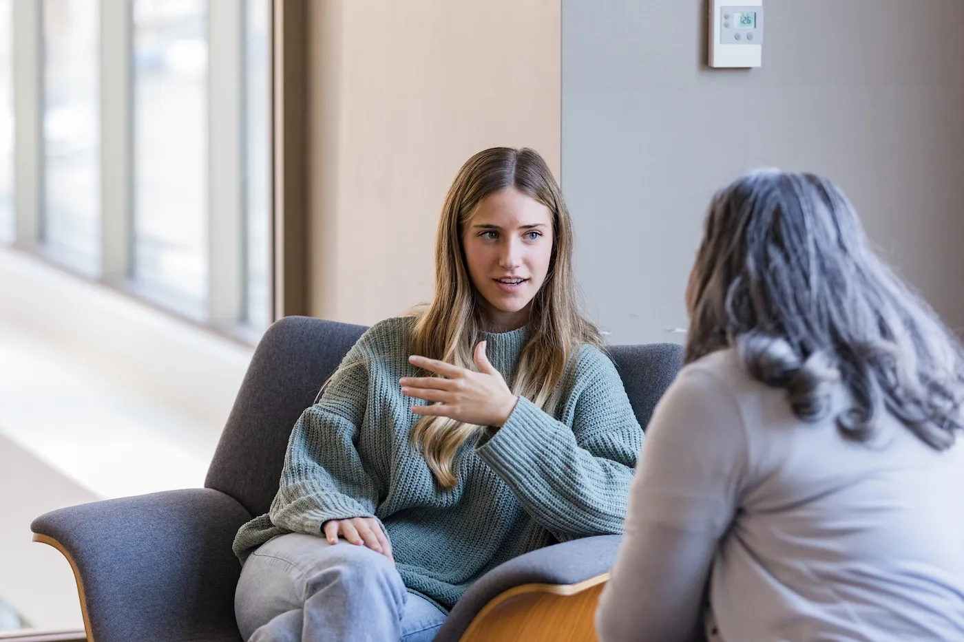 A young adult female talks to a friend about money. They are sitting on a couch.