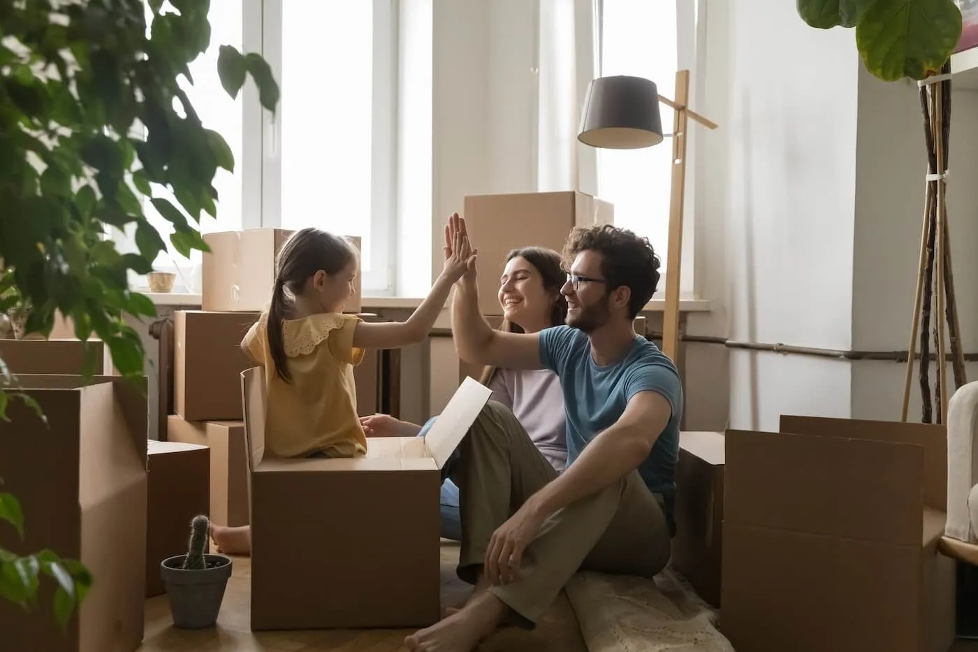 A happy family of three in their new house surrounded by boxes, a girl giving a high five to her father