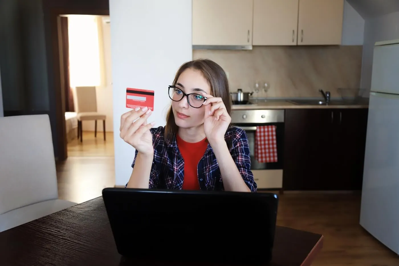 A young woman wearing glasses is looking curiously at her credit card