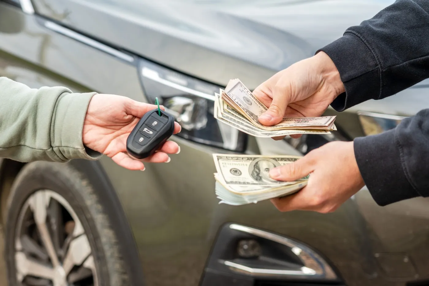 Two people exchange cash for car keys in the process of buying a car.