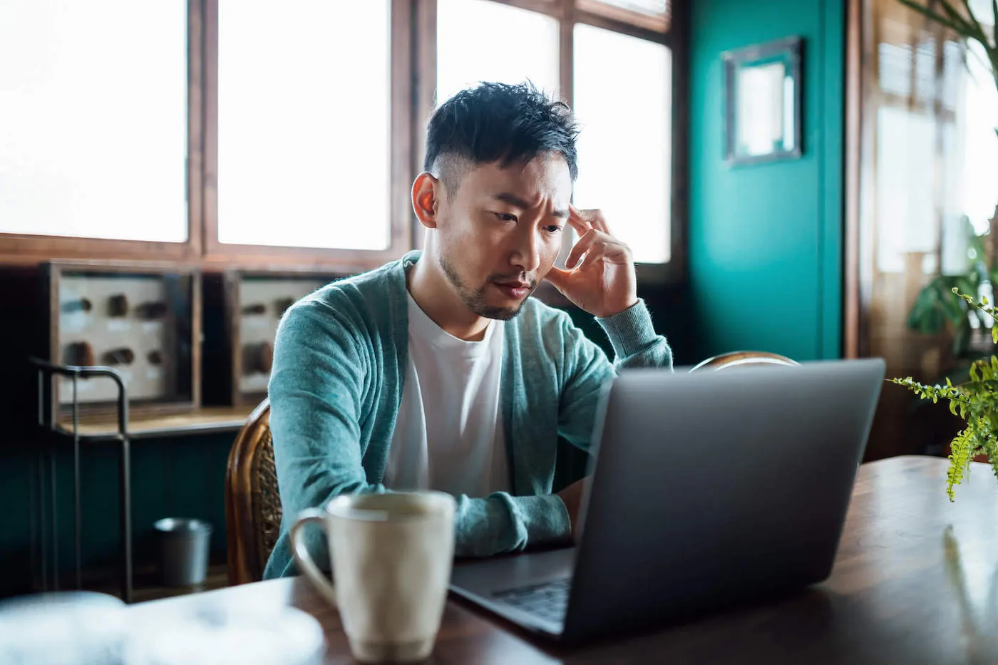 Pensive man staring at laptop screen while seated indoors.