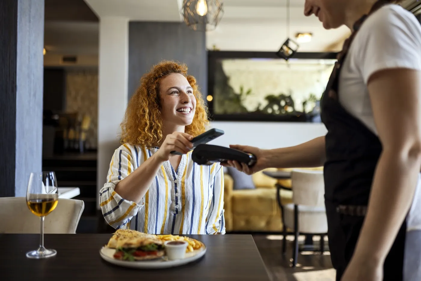 Young woman making payment with virtual credit card in restaurant.