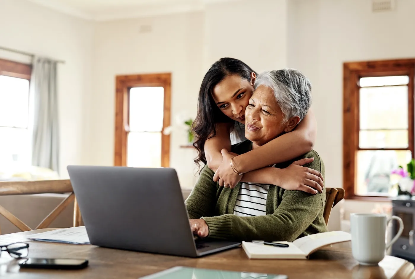 Cropped shot of a young woman hugging her grandmother before helping her with insurance on a laptop.