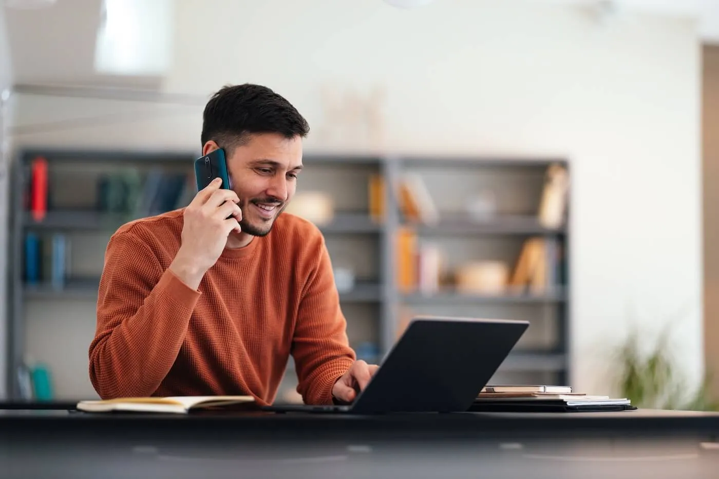 Smiling man making a phone call while using a laptop