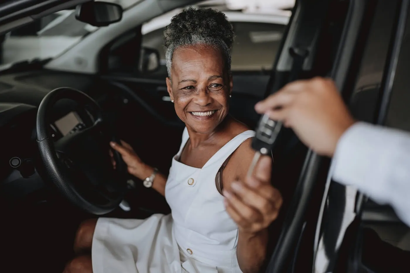 Smiling senior woman is sitting in the rental car and taking the car keys from the agent