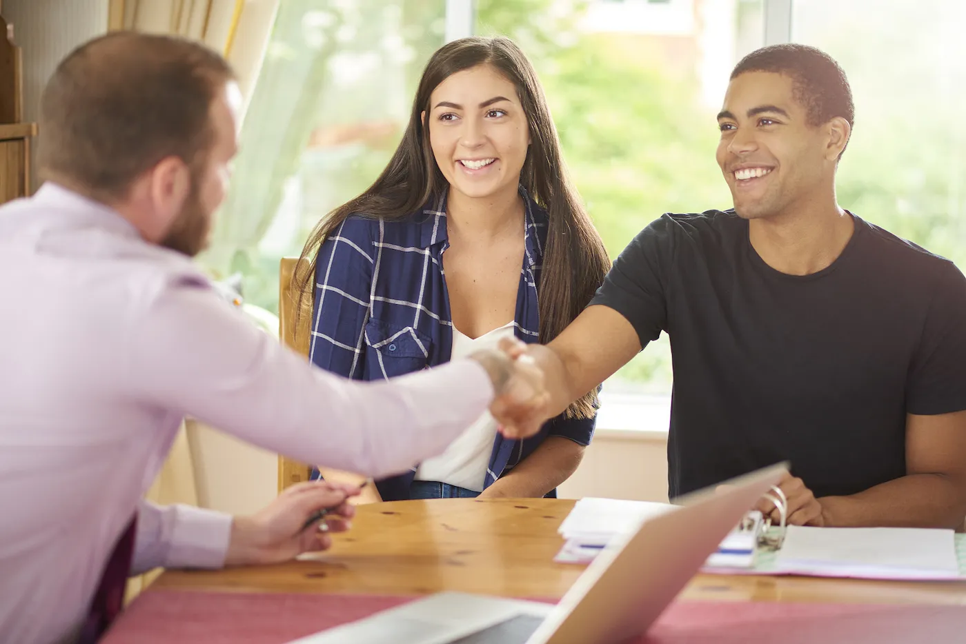 Two roommates sit in their dining room and negotiate rent with their landlord.