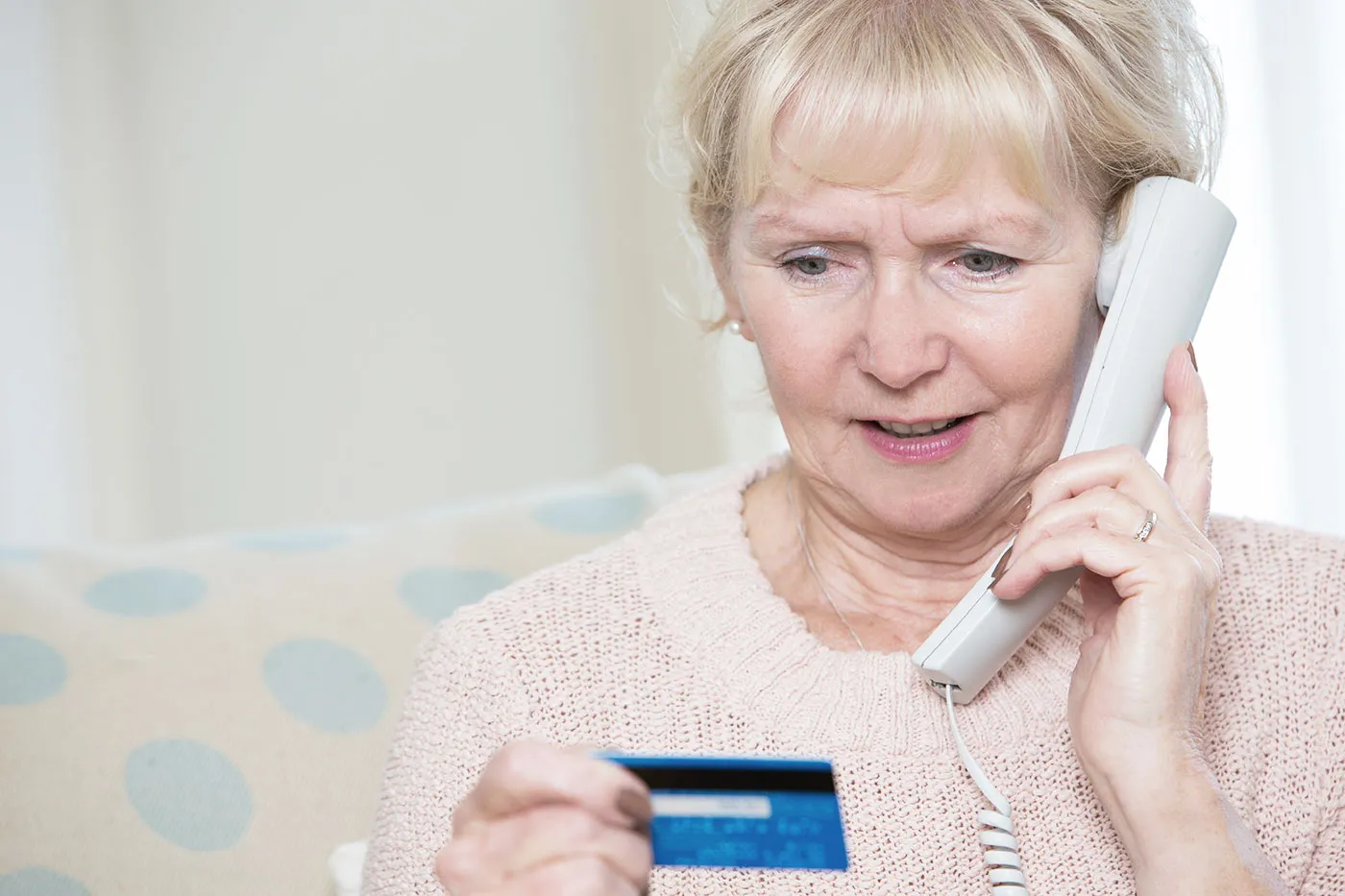 elderly woman in light pink shirt holding a phone and looking at a card