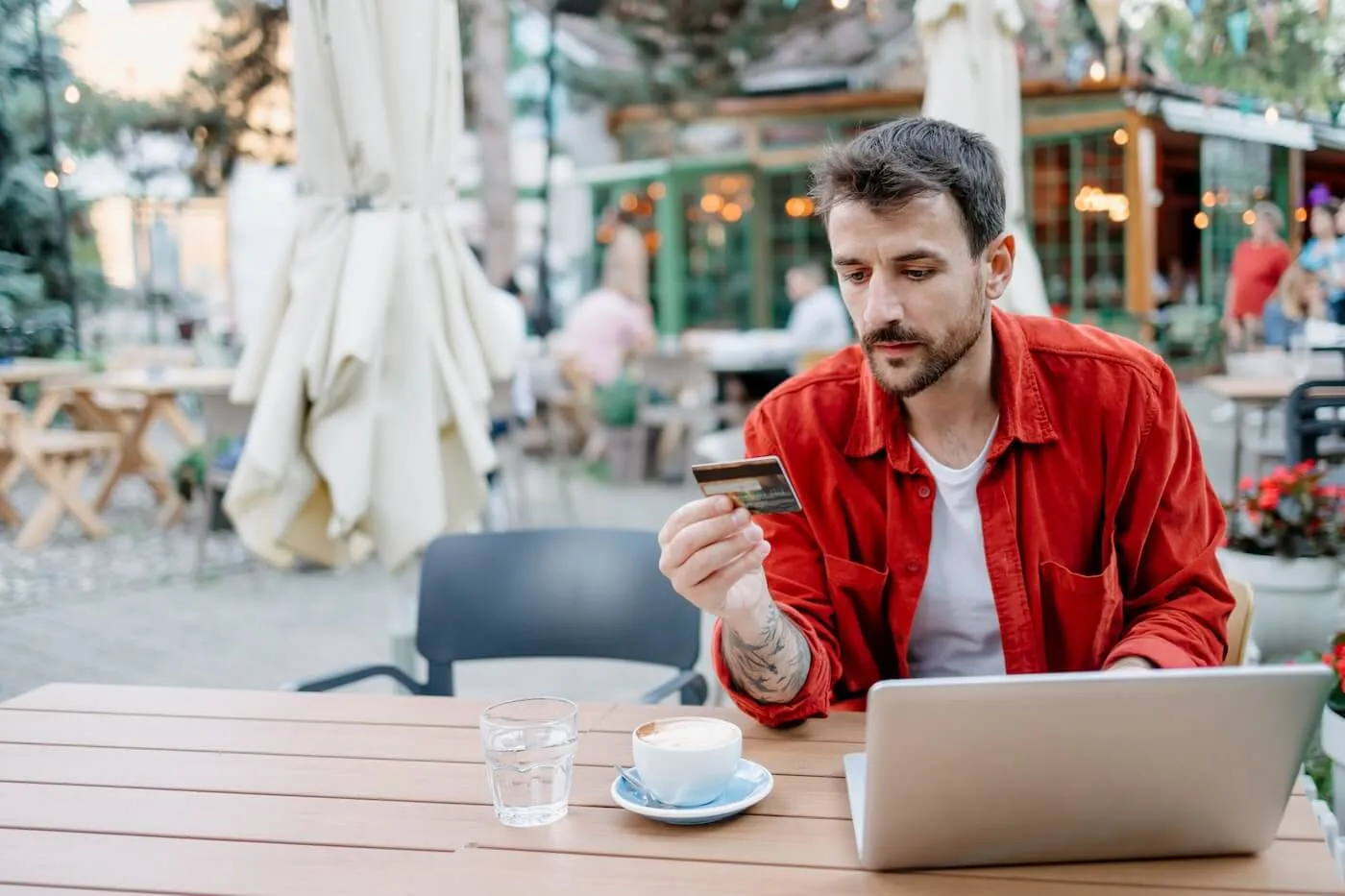 Man with a laptop is using his credit card while having a coffee in the cafe