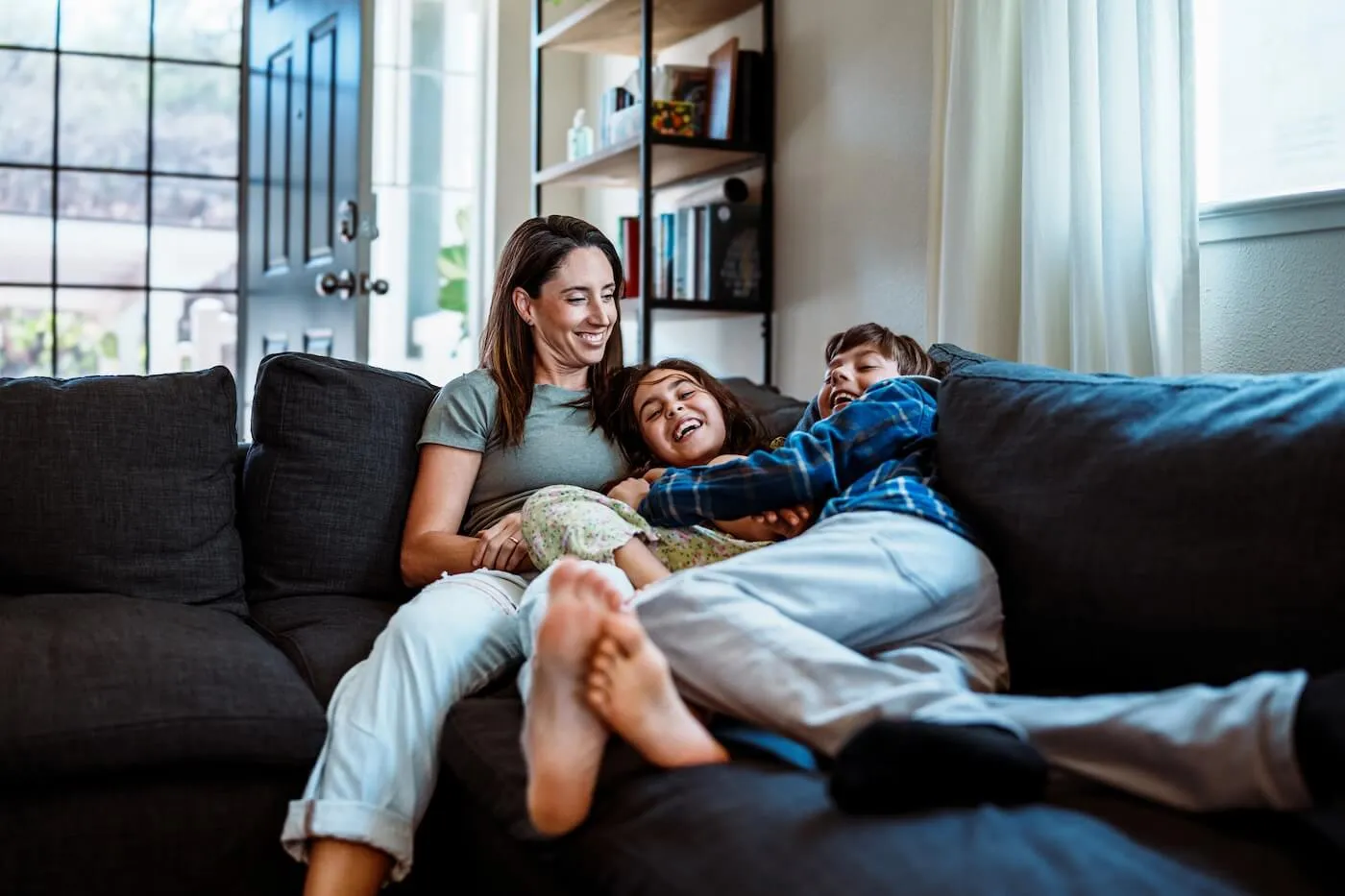 A woman with 2 kids are having fun on the couch