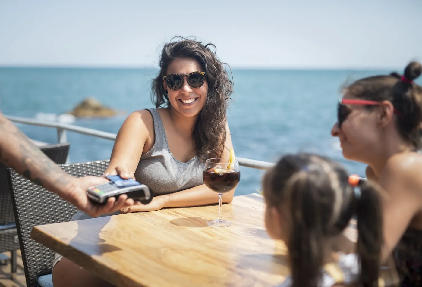 Happy female friends making payment on the beach in summer sea restaurant.