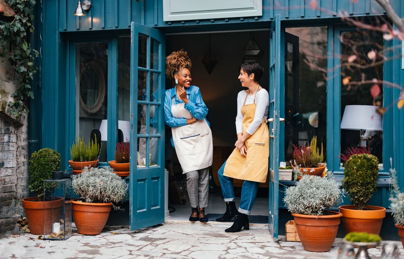 Happy woman and her employee talking and laughing while standing at door of the store.