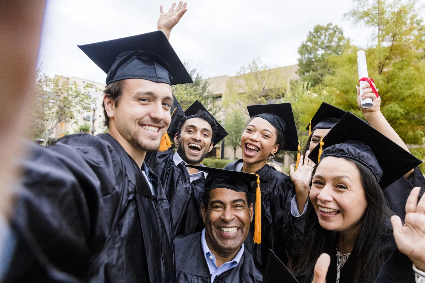 A smiling group of recent college graduates takes a group selfie in their caps and gowns.