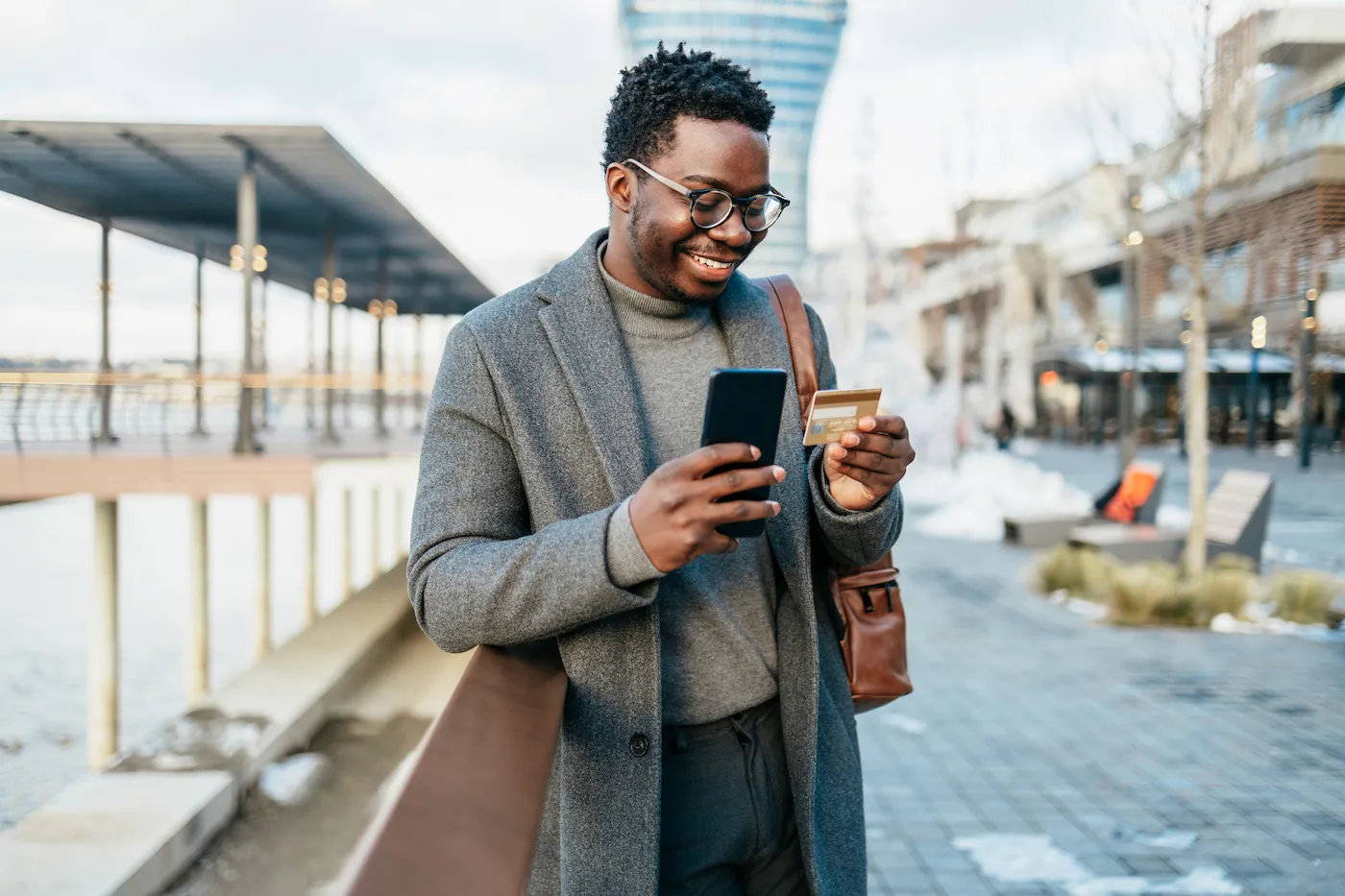 Smiling man on city street uses his phone and credit card.