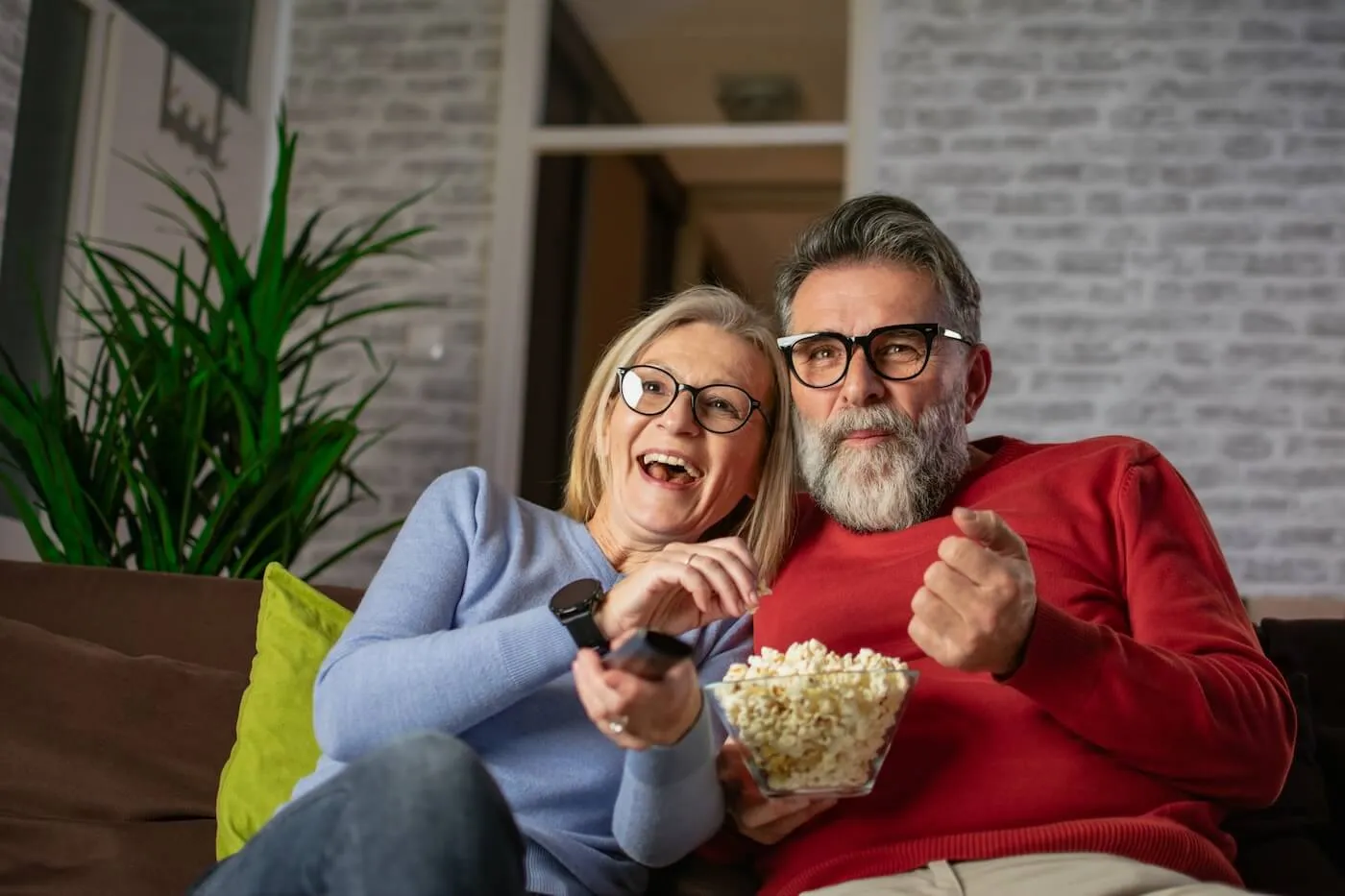 Happy mature couple sitting on a couch with popcorn while watching a movie