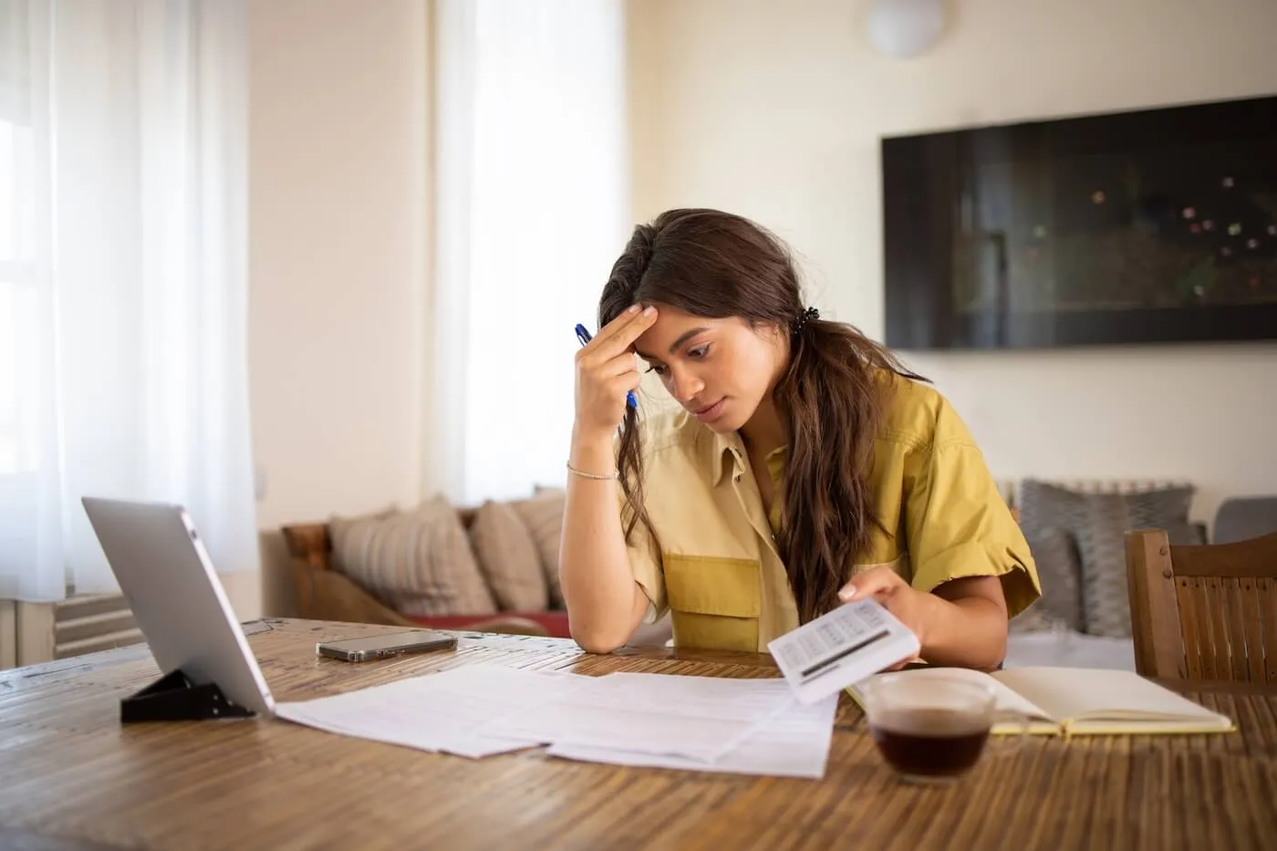 Concerned young woman reviewing her mail and making calculations while using her laptop in the living room