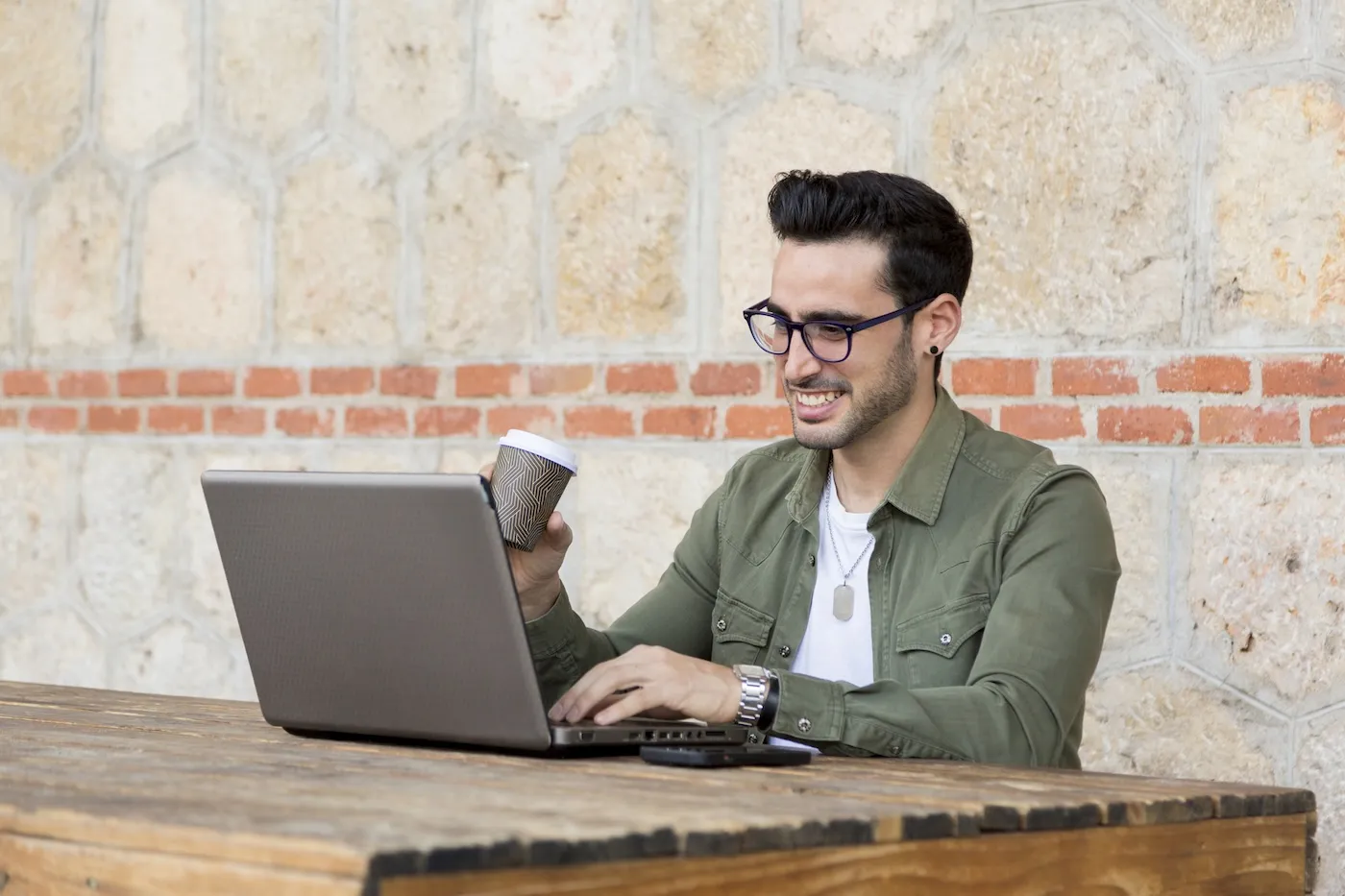 Man drinking coffee while working with a laptop sitting on a terrace.