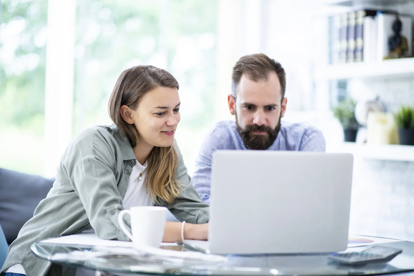 A young couple sits at their home dining table with a laptop an calculator, reviewing their loan options.